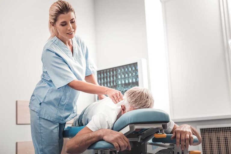 A chiropractor gently examines an adult patient's lower back in a bright clinic room.